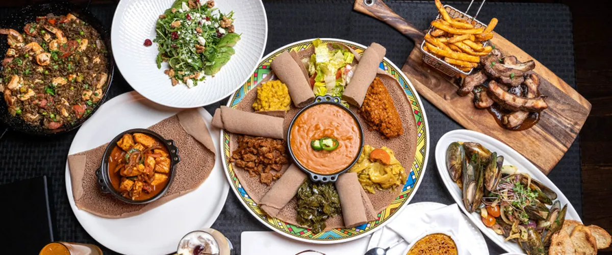 Delicious spread of classic Ethiopian and Caribbean cuisine laid out across a table with black mats underneath.