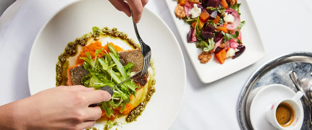 Delicious spread of Viennese food from the restaurant Grunauer spread across a table as a customer digs in with a fork and knife.