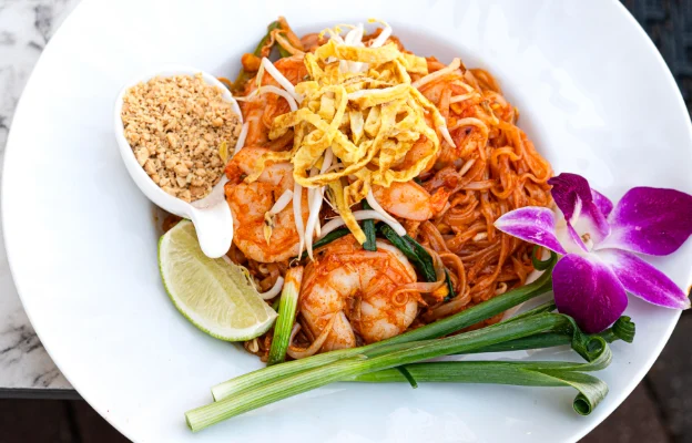 Delicious Seafood Pad Kee Mow, accompanied by crumbs and a lime in a white bowl.