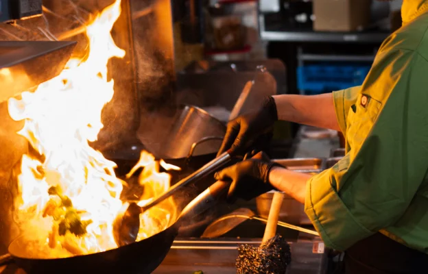 Chef at Aqua Penny’s cooks food in a flaming skillet with black gloves on.