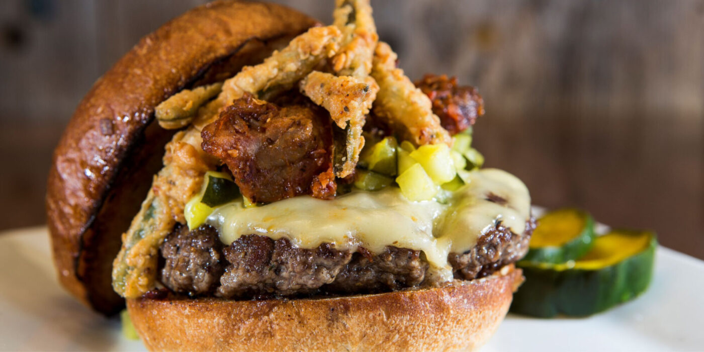 A burger between two buns topped with cheese, fried pickles, and regular pickles.