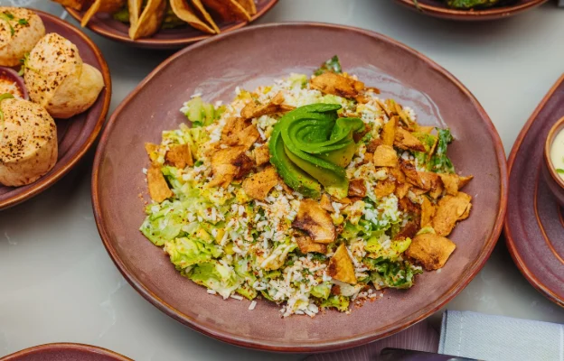 A large bowl featuring meat, lettuce, seasoning, and a twisted avocado at the center.