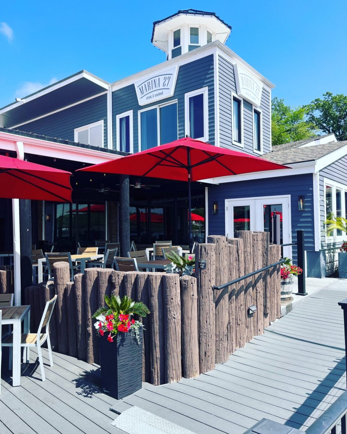 The exterior view of the Marina 27 restaurant in Kansas City painted blue with red umbrellas and flower decor