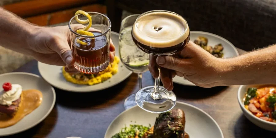 Two customers clink their glasses together to celebrate over a table full of delicious foods.