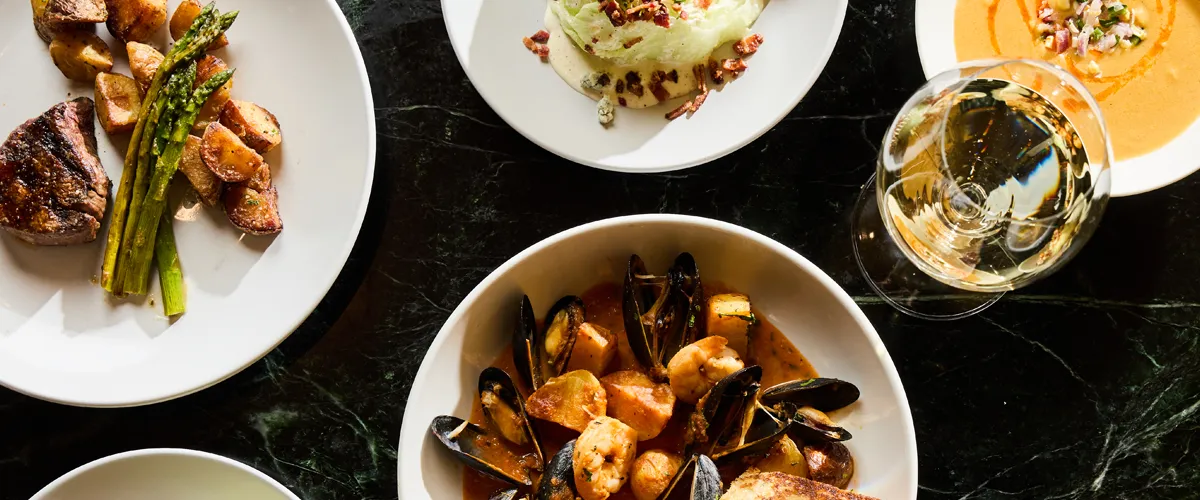 A delicious spread of high-end surf and turf including steak, shrimps, mussels, paired with a glass of wine.