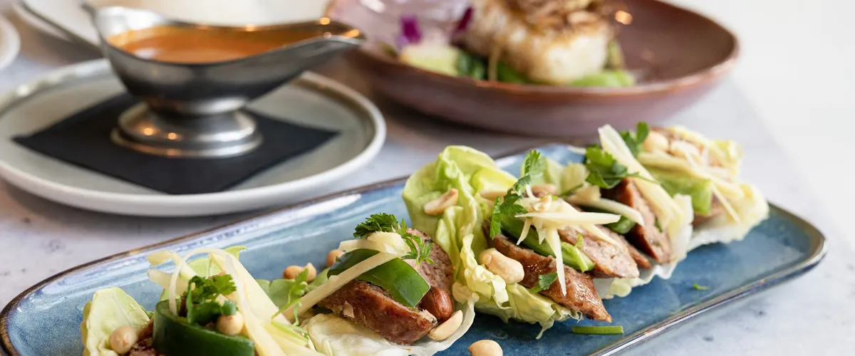 Lettuce wraps with meat, bell peppers, and other vegetables inside with a sauce in the background.