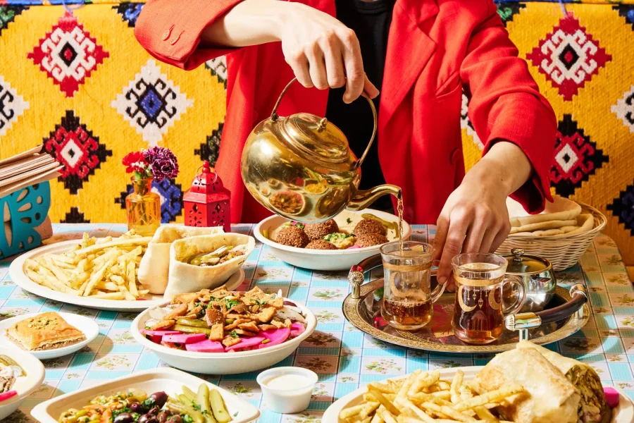 Tea being poured into a glass on a table alongside a delicious spread of Mediterranean food.