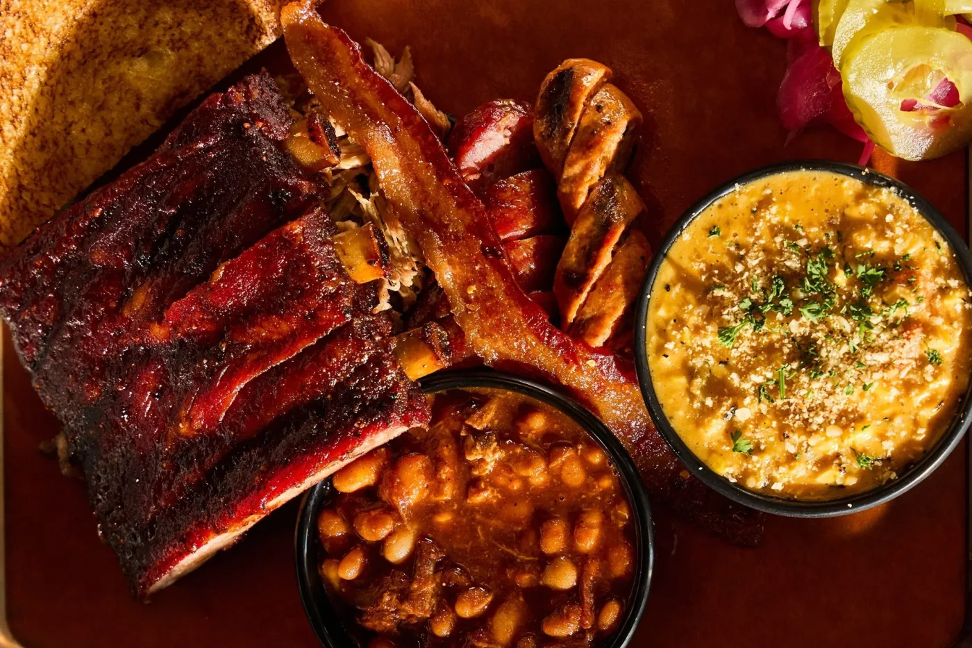 An array of barbecue foods including ribs, baked beans, sausages, and mac-and-cheese.