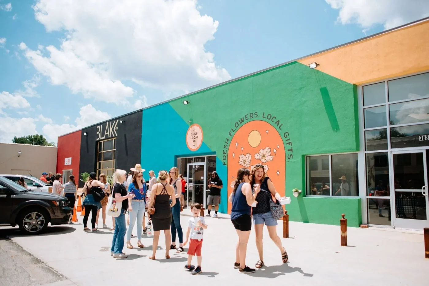 A large group of customers hang out in front of two local KC shops including a flower shop and a retail gift shop.