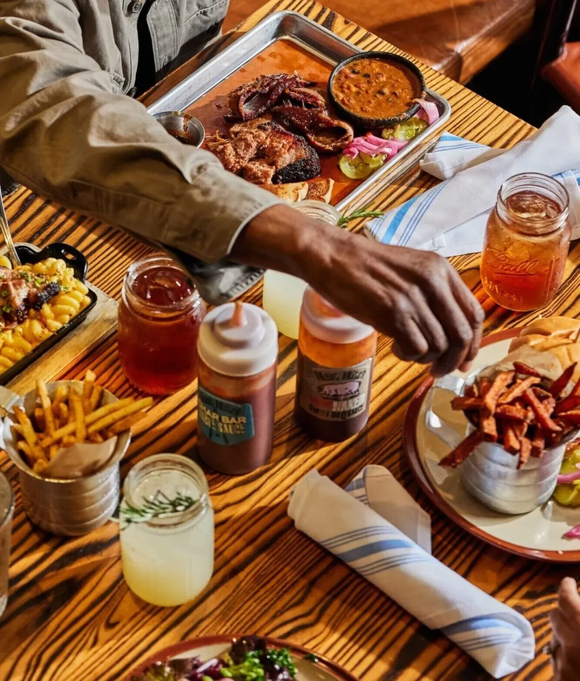 Customers enjoy a spread of different barbecue foods along with various barbecue sauces on the table